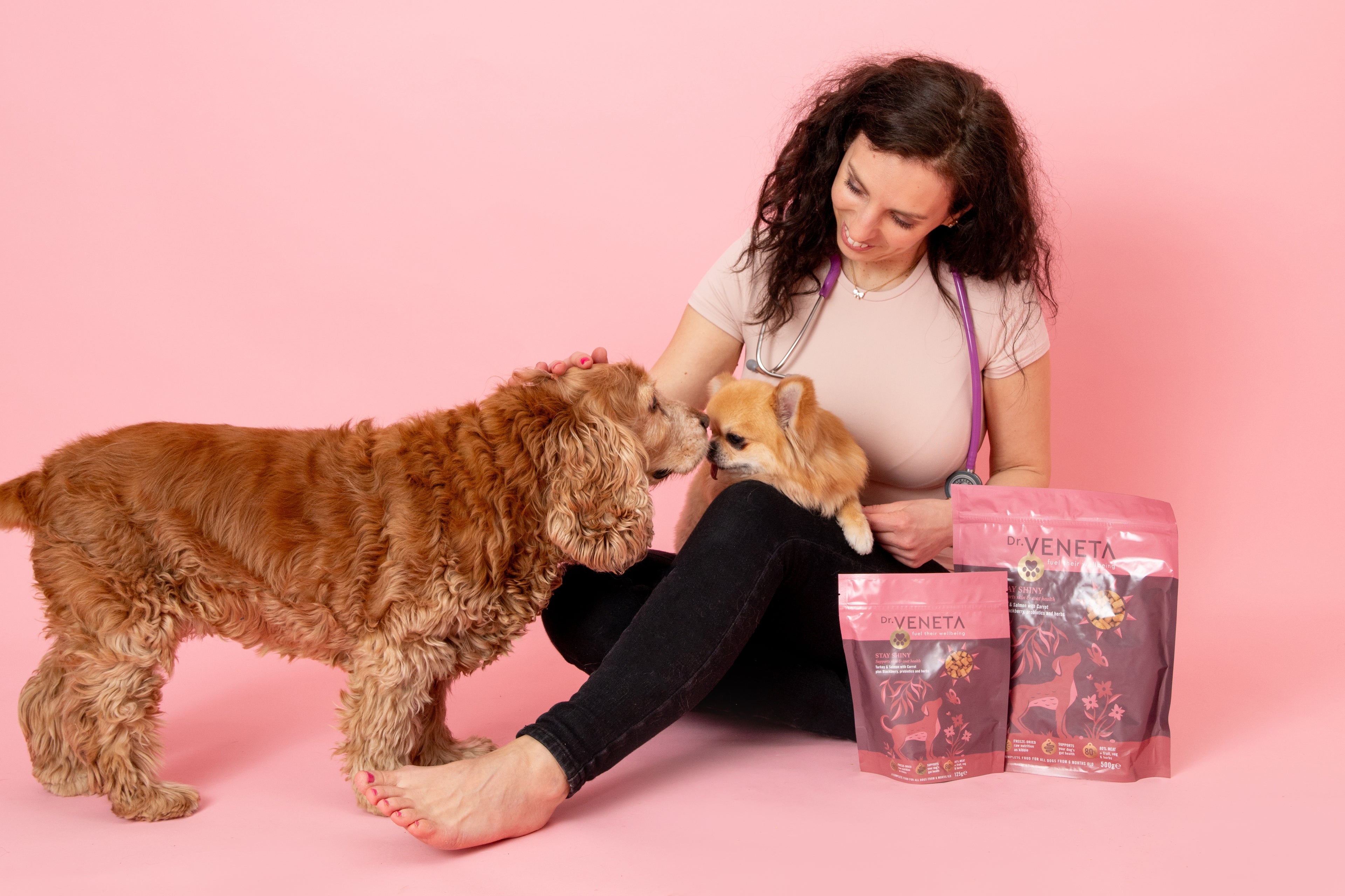 Dr. Veneta founder with two dogs and Dr. Veneta dog food products on a pink background
