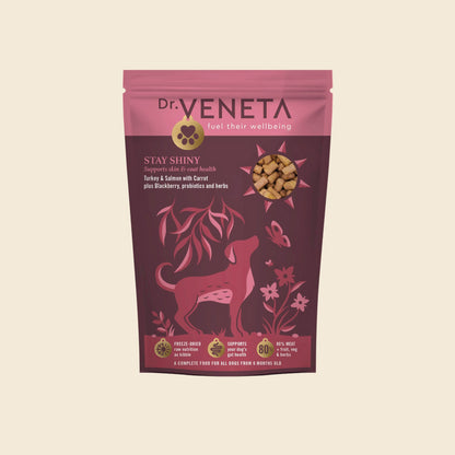 A stand-up pouch of Dr. Veneta Stay Shiny dog food, featuring a pink and dark magenta design with a dog silhouette and a clear window showing the kibble inside, set against a solid cream background.