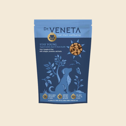A stand-up pouch of Dr. Veneta Stay Young dog food, featuring a blue and navy design with a dog silhouette and a circular image of the kibble, set against a solid beige background.